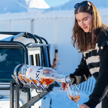 Load image into Gallery viewer, Person pouring wine from a bottle into a glass outdoors with mountains in the background