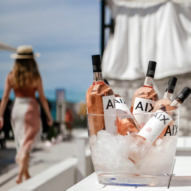 Bottles of AIX rosé wine on ice with a blurred background of people and a boat.