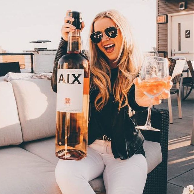 Woman holding a Magnum bottle of AIX rosé wine on a rooftop with a cityscape background