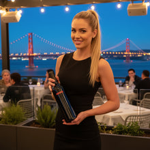 Load image into Gallery viewer, Woman holding a bottle of Bottle of Saldo Zinfandel red wine with a cityscape and bridge in the background