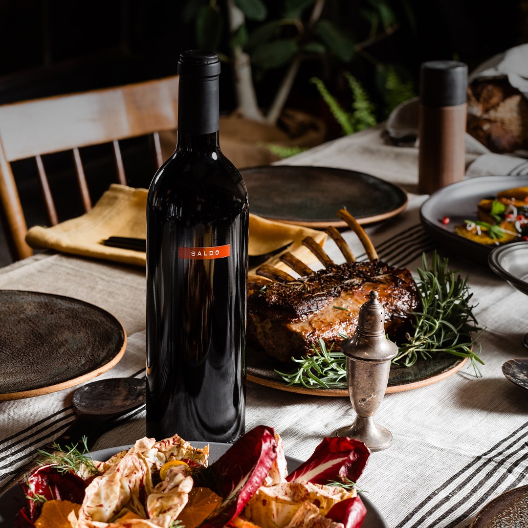 Load image into Gallery viewer, Bottle of Saldo Zinfandel red wine on dinner table next to grilled lamb rack