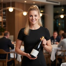 Load image into Gallery viewer, Woman holding a bottle of Sam Harrop Onetangi Waiheke Island syrah wine in a restaurant setting