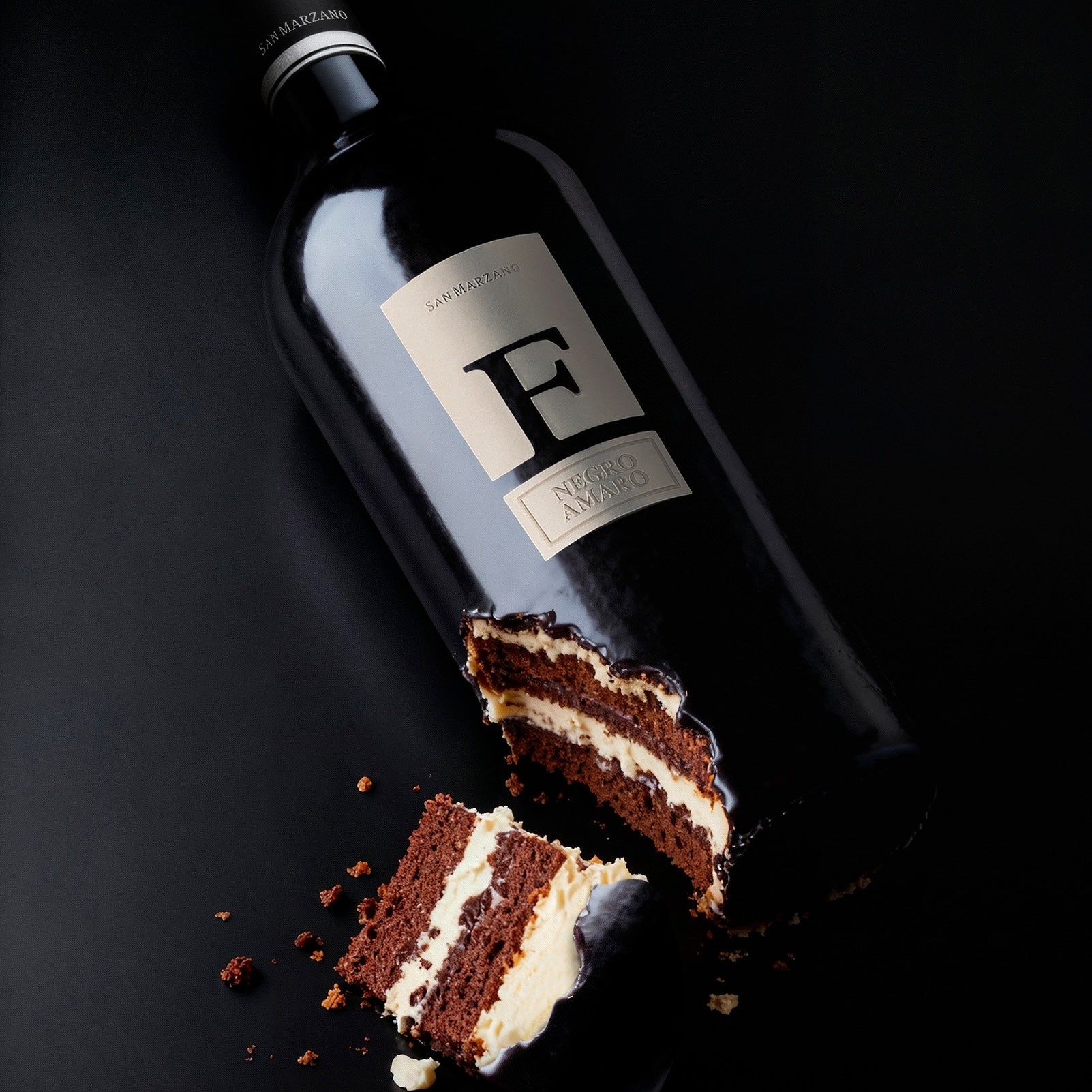 Load image into Gallery viewer, Bottle of San Marzano F Puglia Negroamaro wine next to a piece of chocolate cake on a dark background