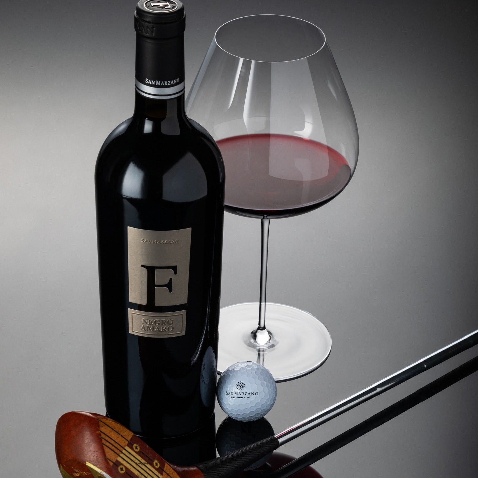 Load image into Gallery viewer, San Marzano F Puglia Negroamaro wine bottle, glass with red wine, golf club, and golf ball on a reflective surface