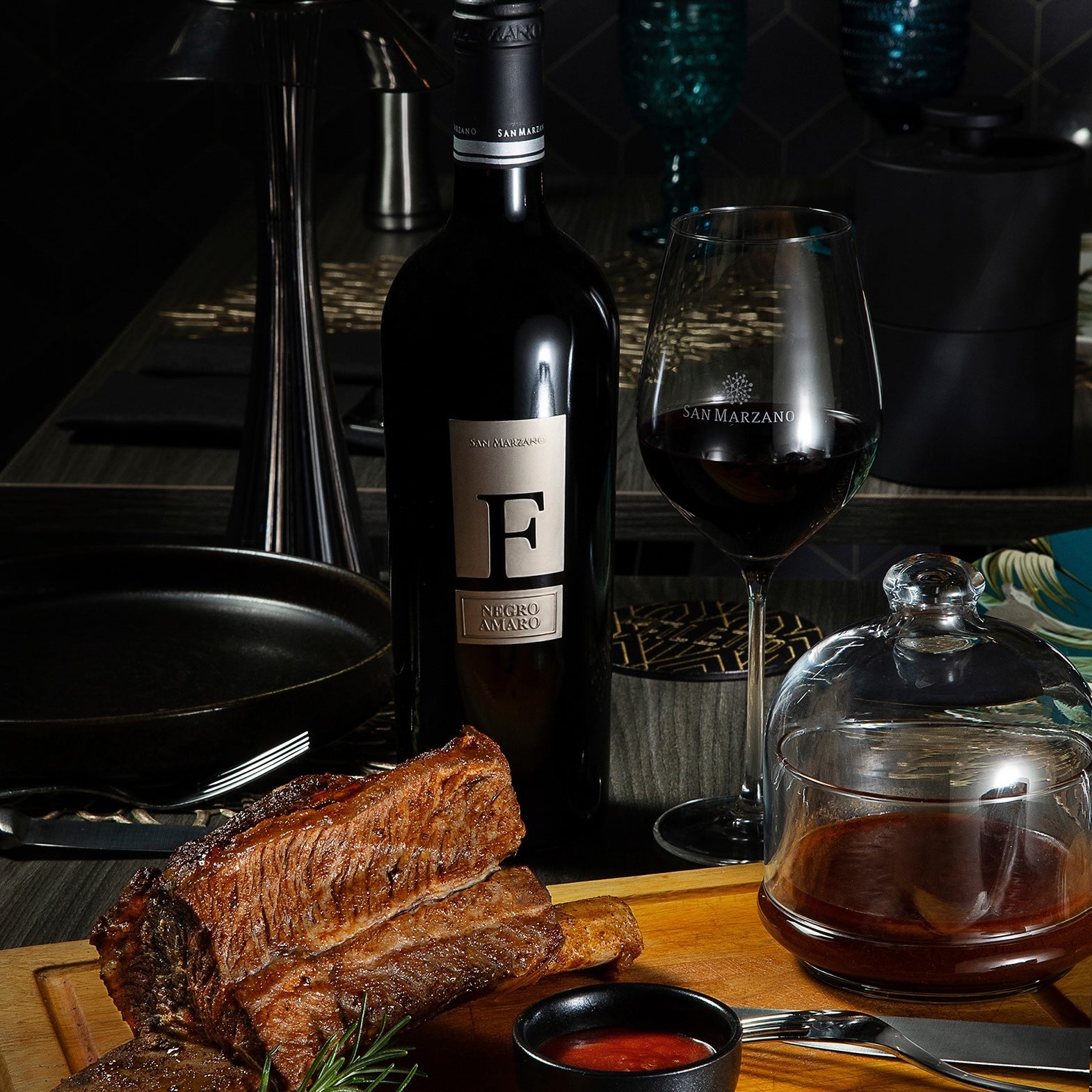 Load image into Gallery viewer, A bottle of San Marzano F Puglia Negroamaro red wine next to a half-full red wine glass and a bbq steak beside