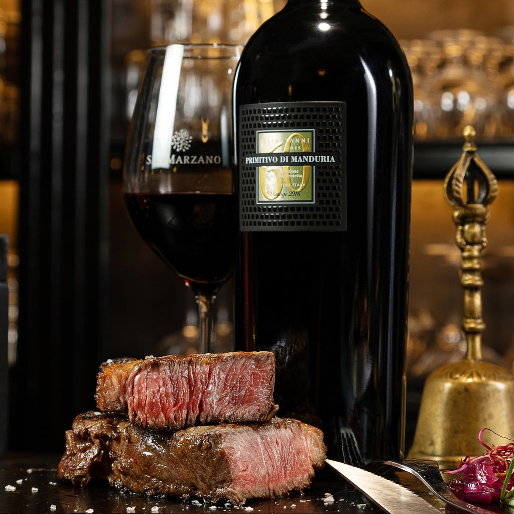 A bottle of San Marzano Sessantanni Primitivo with a wine glass and beef steak in front of it