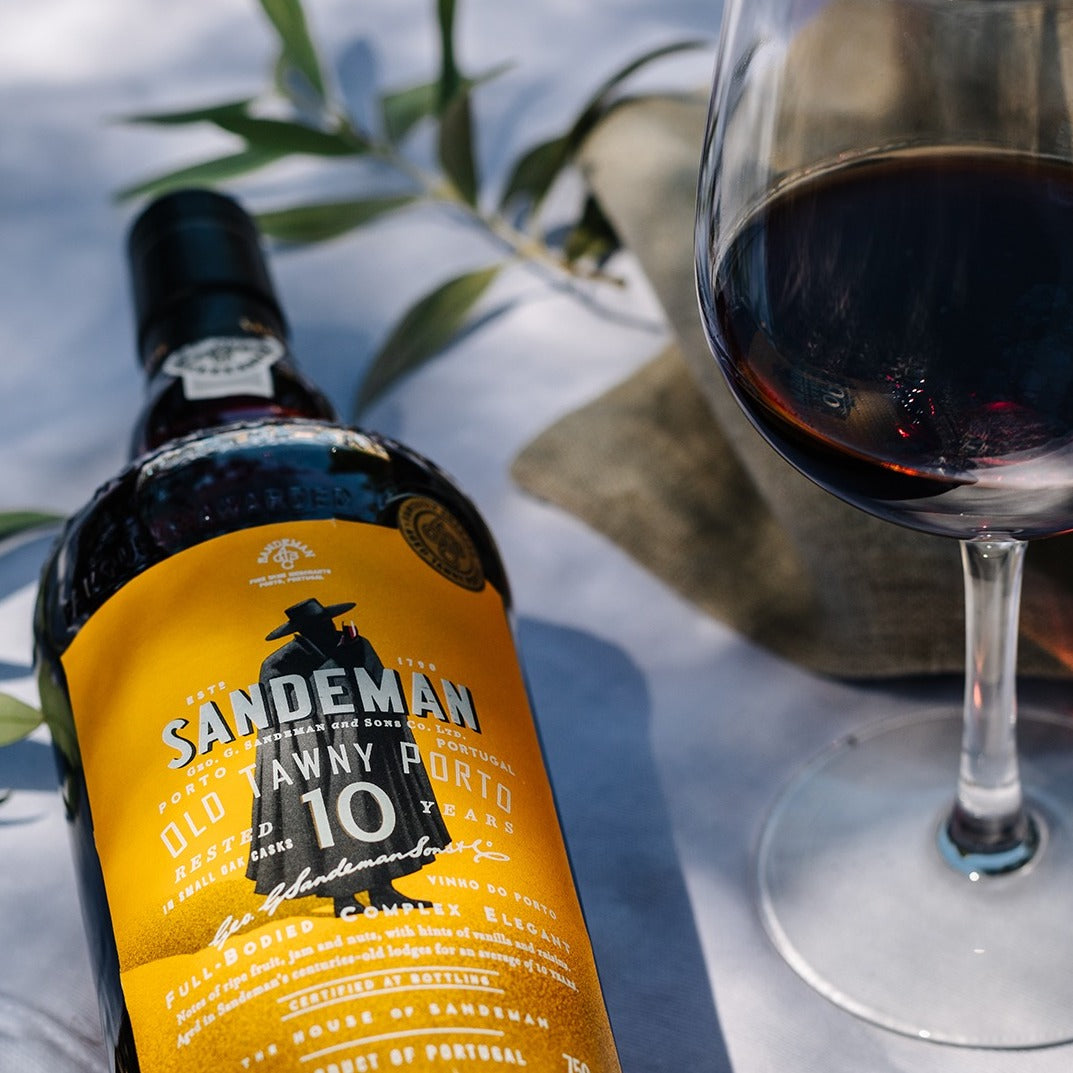 Load image into Gallery viewer, A bottle of Sandeman port and a glass on a white table cloth with some greenery