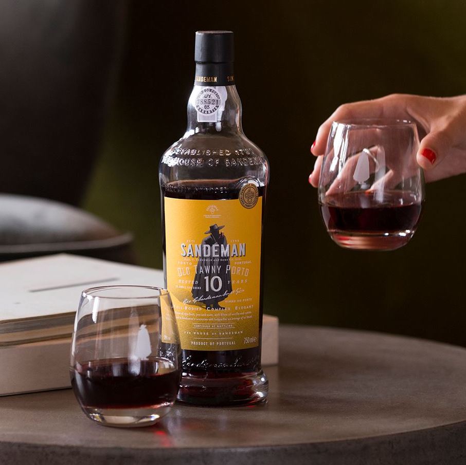 Load image into Gallery viewer, A hand holding a glass of port and a bottle of port on a marble table with a green background