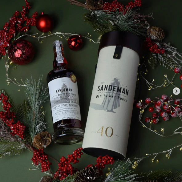 Sandeman Old Tawny Porto bottle and box on a festive green background with red berries and greenery.