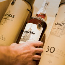 Load image into Gallery viewer, Person holding a Sandeman Old Tawny Porto bottle with packaging in the background.