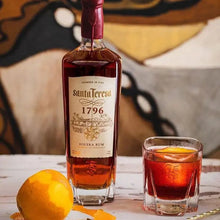 Load image into Gallery viewer, Bottle of Santa Teresa 1796 rum with a glass of red cocktail on a wooden surface.