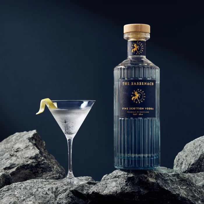 Load image into Gallery viewer, Bottle of The Sassenach Fine Scottish vodka and a cocktail on rocks with a dark background