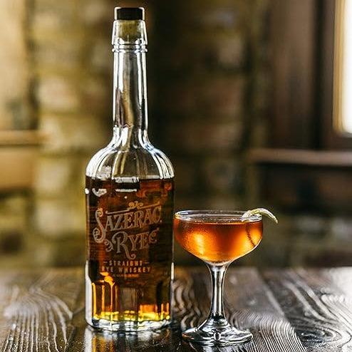 Load image into Gallery viewer, Bottle of Sazerac Rye whiskey and a cocktail glass with a drink on a wooden surface.