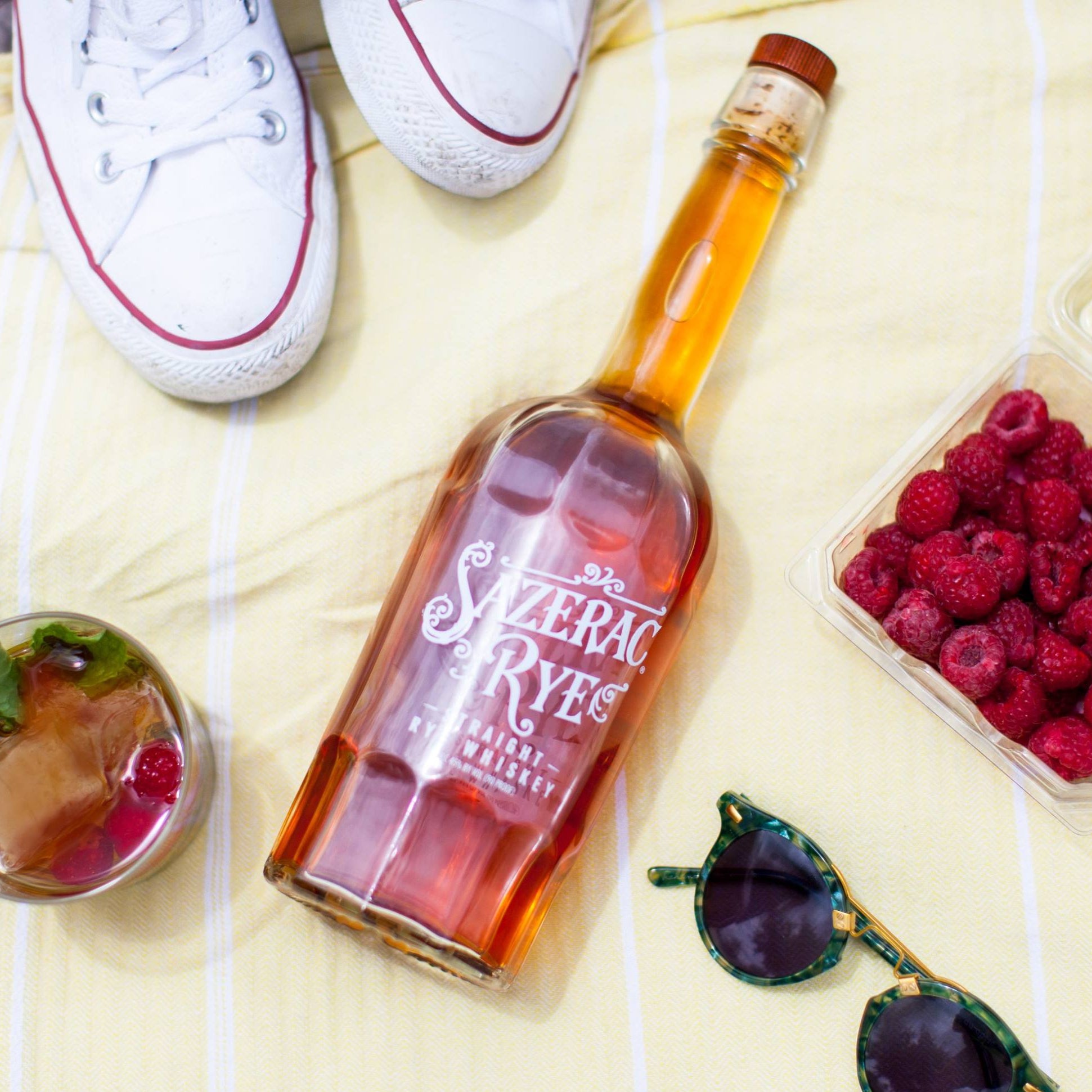 Load image into Gallery viewer, Bottle of Sazerac Rye whiskey with a glass of cocktail, raspberries, and sunglasses on a yellow surface