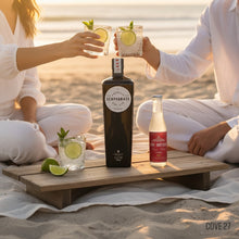 Load image into Gallery viewer, Two people sitting on a beach with drinks and a bottle of Scapegrace Classic Gin on a wooden tray.