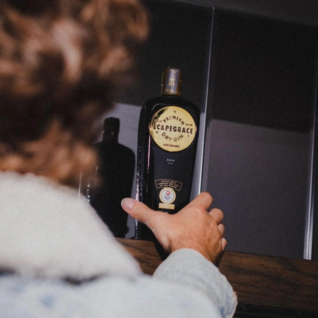 Person holding a bottle of Scapegrace Gold gin with a blurred background