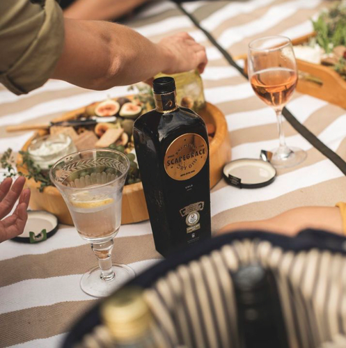 Bottle of Scapegrace Gold Gin on a table with a glass and food items