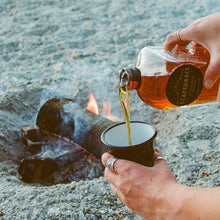 Load image into Gallery viewer, Person pouring whisky from a bottle of Scapegrace Vanguard Single Malt Whisky into a cup by a campfire on a beach.