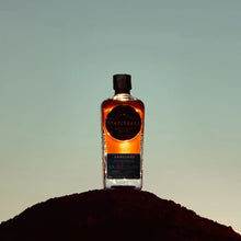 Load image into Gallery viewer, Bottle of Scapegrace Vanguard Single Malt Whisky on a small hill with a gradient sky