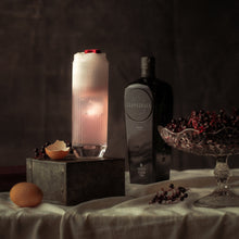 Load image into Gallery viewer, Scapegrace Black Gin bottle and a pink cocktail in a highball glass on a table with decorative items and a lit candle.