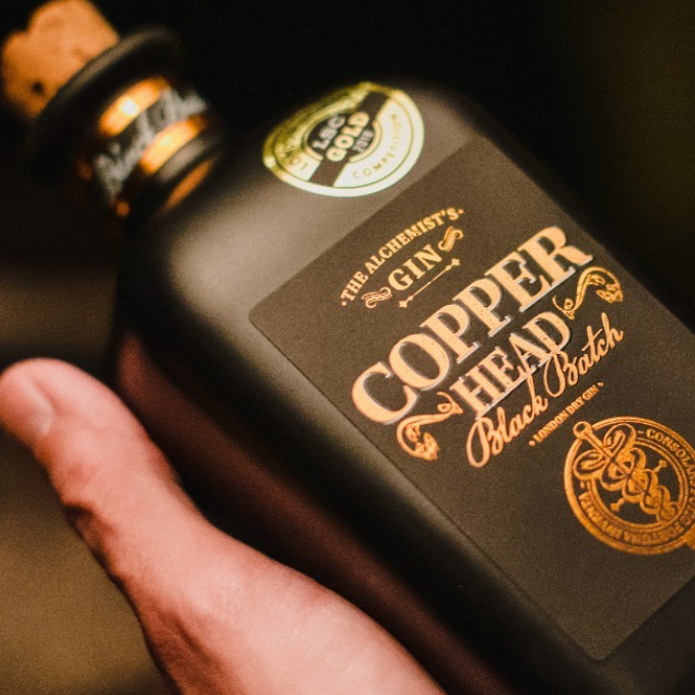 Load image into Gallery viewer, Bottle of Copperhead Black Batch Gin held by a man's hand with a dark background