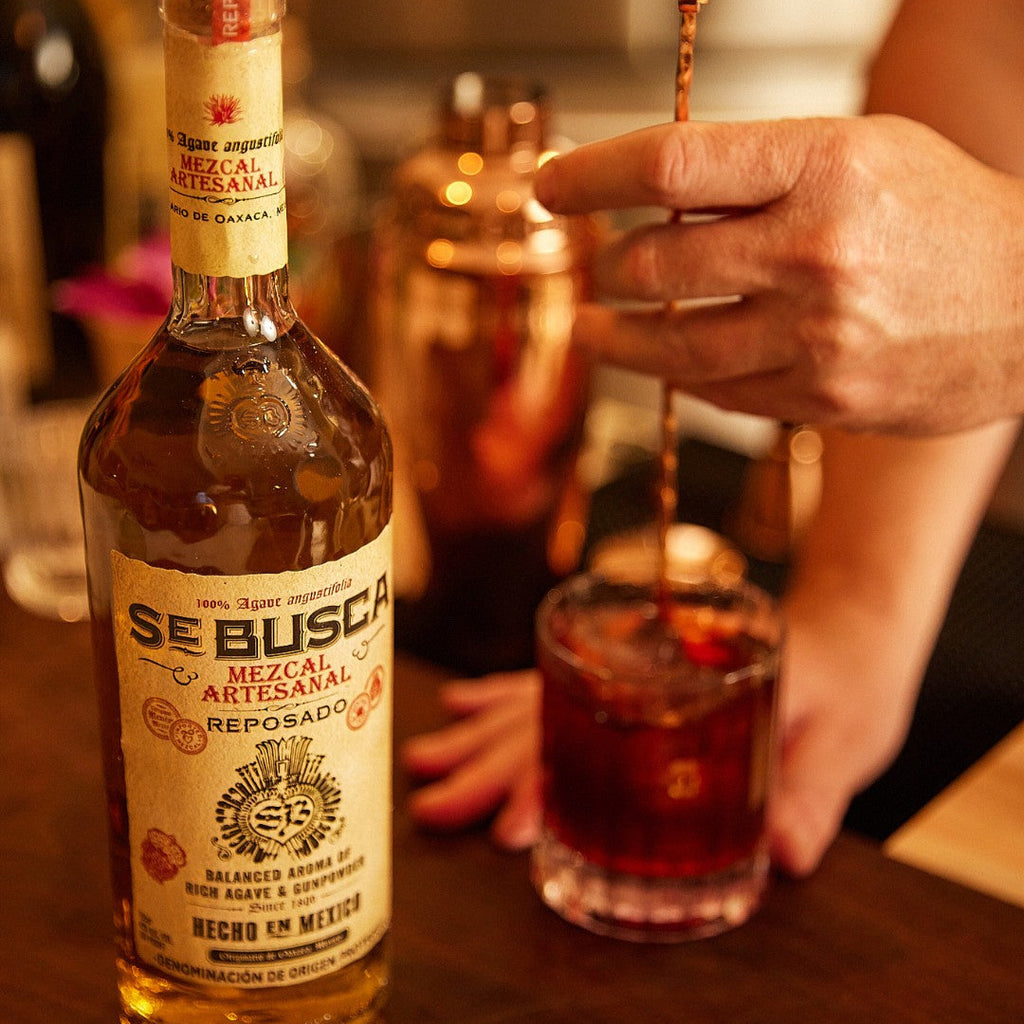 Bottle of Se Busca Mezcal Reposado with a glass of mezcal on a bar counter.