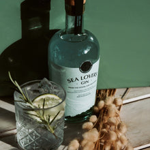 Load image into Gallery viewer, Bottle of Sea Lovers Gin with a glass of gin and tonic on a wooden surface.
