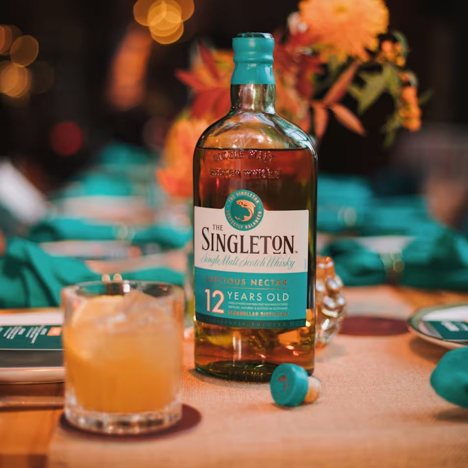 Load image into Gallery viewer, Singleton of Dufftown 12 Year Old Single Malt Scotch Whisky bottle on a table with a blurred background