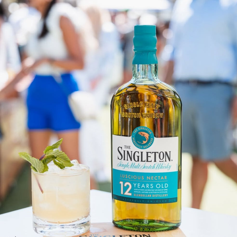 Load image into Gallery viewer, A bottle of Singleton of Dufftown 12 Year Old Single Malt Scotch Whisky next to a cocktail with people in the background