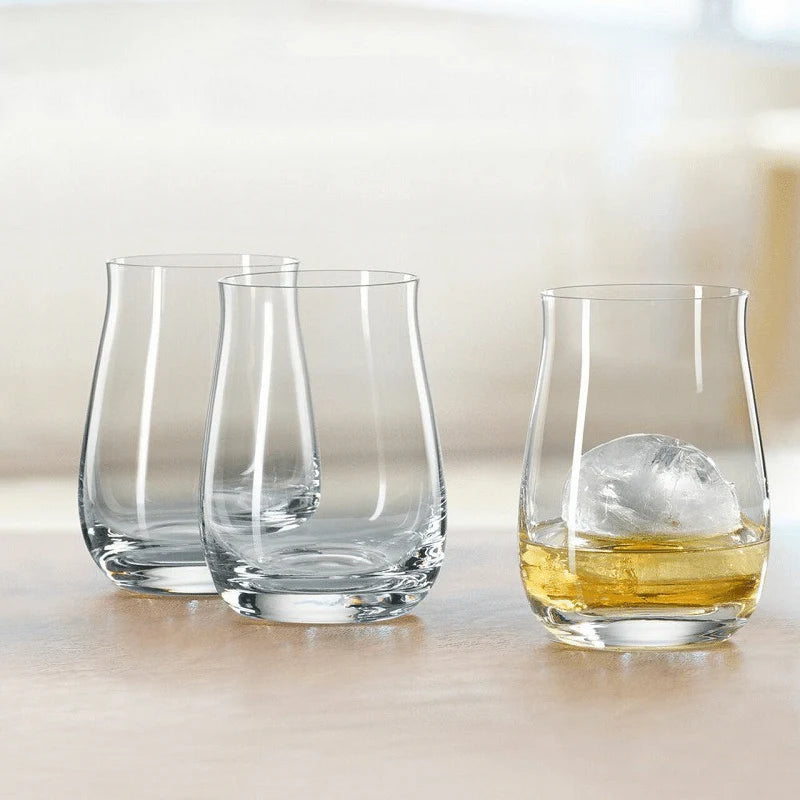 Three clear glasses on a light surface with one containing a small ice cube and liquid.