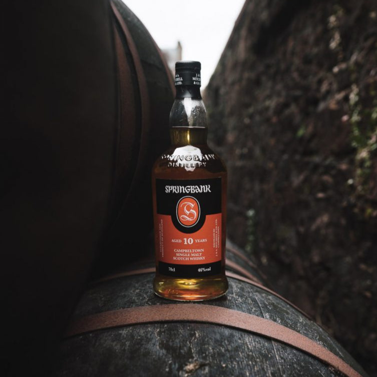 Load image into Gallery viewer, Springbank 10 year old whisky bottle on a   barrel with blurred background