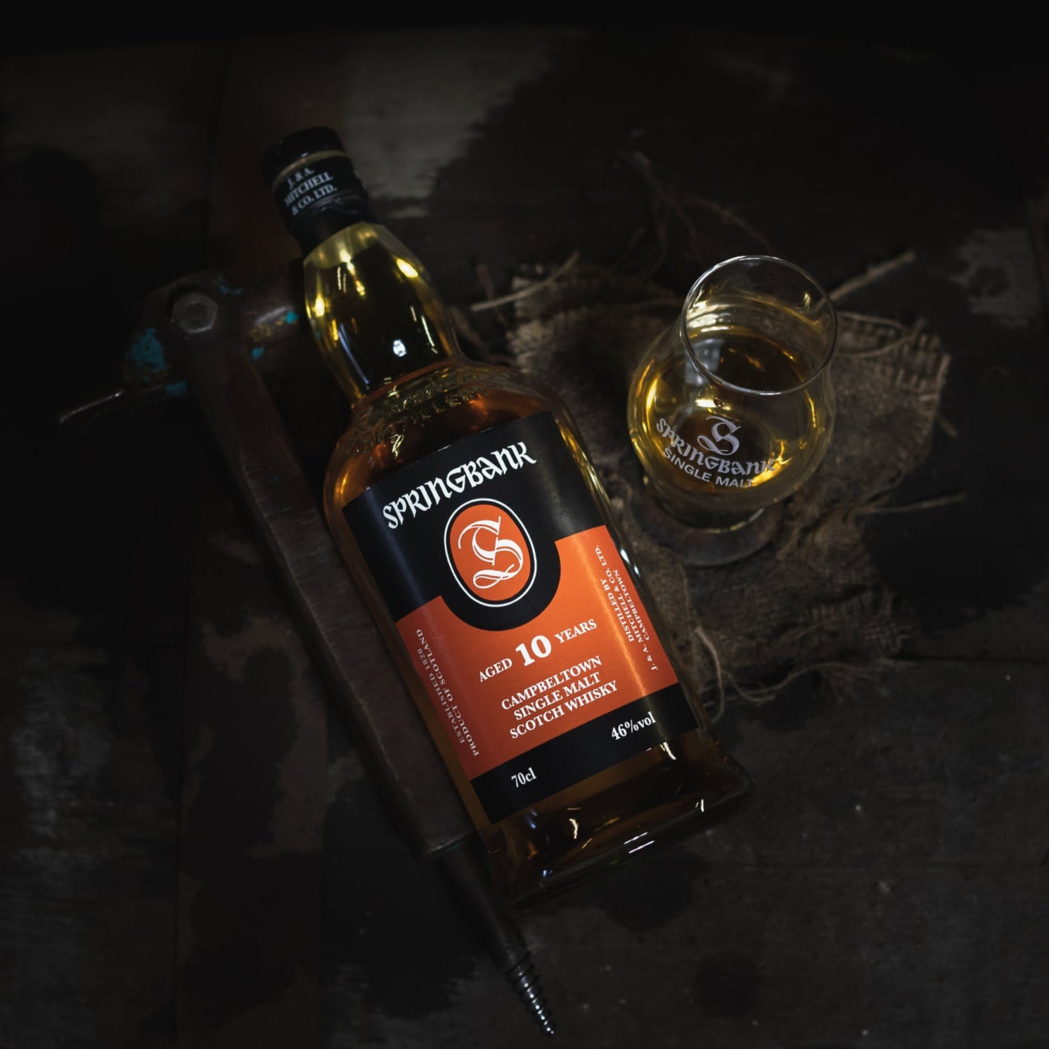 Load image into Gallery viewer, Springbank 10 year old whisky bottle and glass on a dark textured surface
