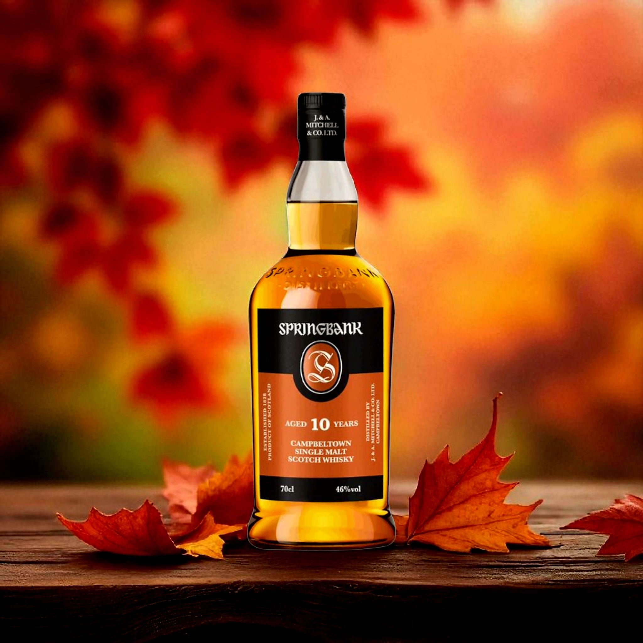 Load image into Gallery viewer, A bottle of Springbank 10 Years Single Malt Scotch Whisky sits on a wooden surface surrounded by autumn maple leaves, with a warm, blurred background of red and orange leaves.