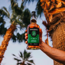 Load image into Gallery viewer, Person holding a bottle of Springbank whisky with palm trees in the background