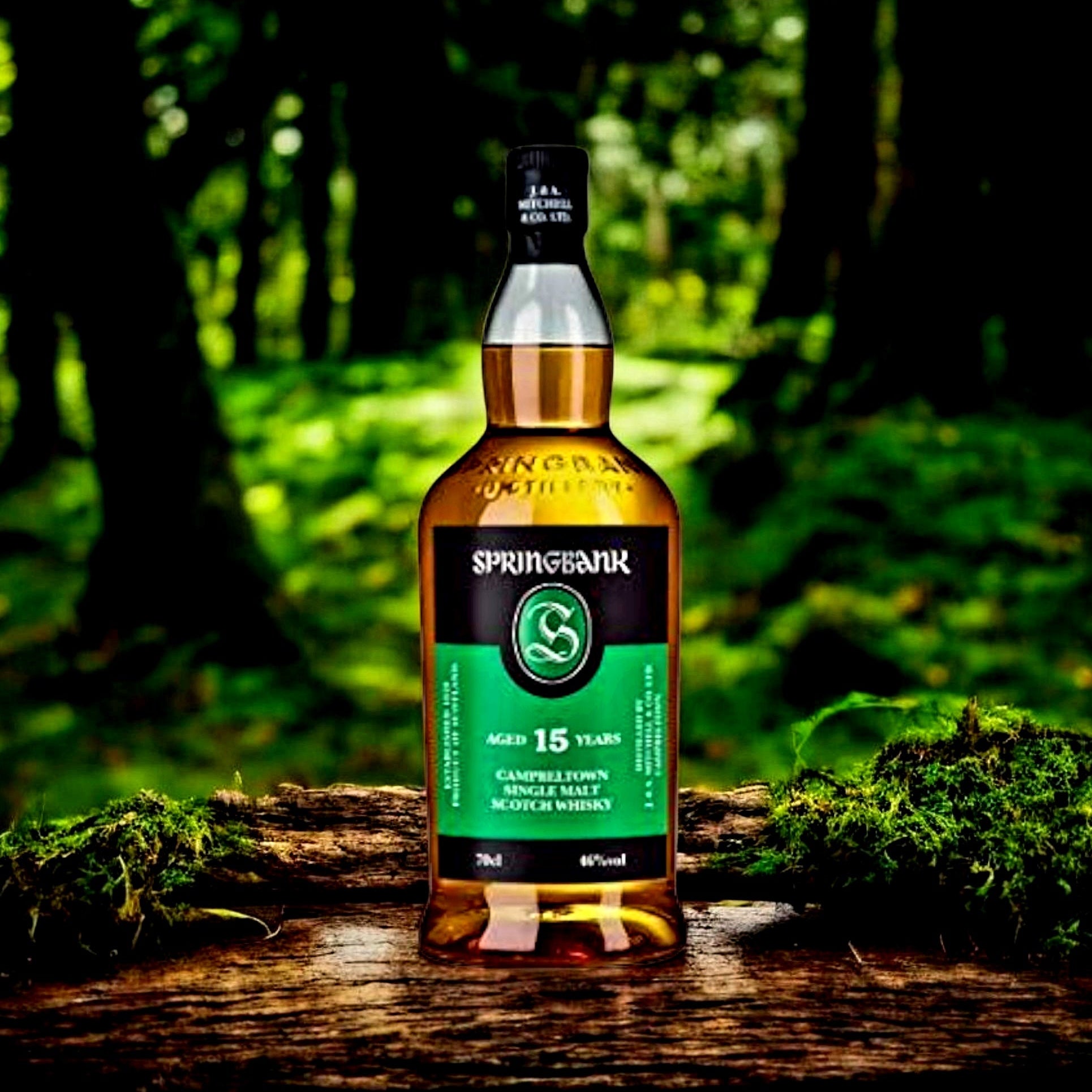 Load image into Gallery viewer, A bottle of Springbank 15 Years single malt Scotch whisky stands on a weathered log in a mossy forest setting. The bottle features a black cap and a green label with white text, set against a blurred background of green woodland.