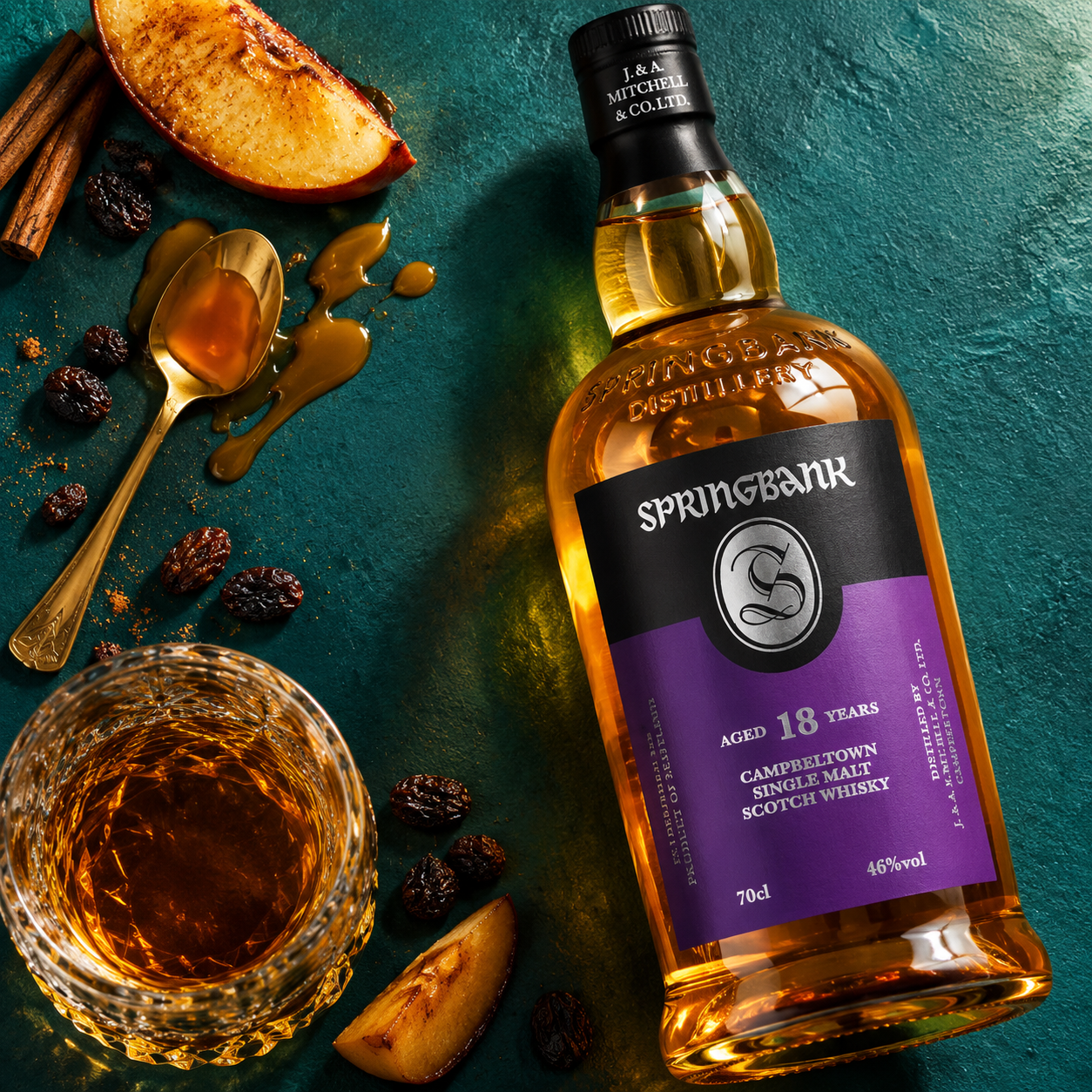 Load image into Gallery viewer, A bottle of Springbank 18 Years Campbelton Single Malt Scotch Whisky is arranged on a dark teal surface with a glass of amber whisky, sliced apple, cinnamon sticks, raisins, and a spoon of honey around it.