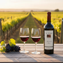 Load image into Gallery viewer, Bottle of St-Hallett-Blackwell-Shiraz wine and two glasses with grapes on a wooden table in a vineyard setting.