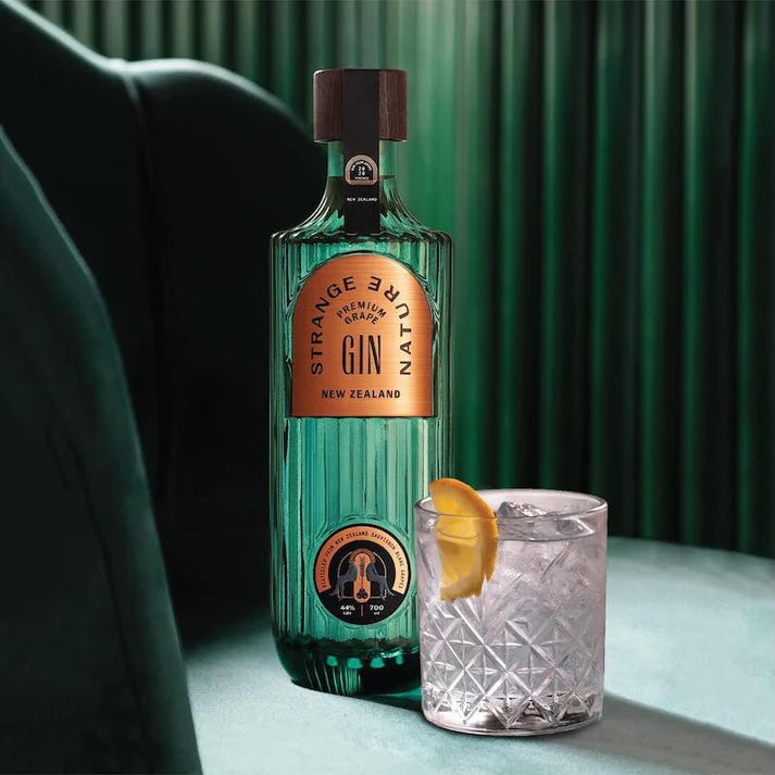 Load image into Gallery viewer, Bottle of Strange Gin with a glass of gin and tonic on a green background
