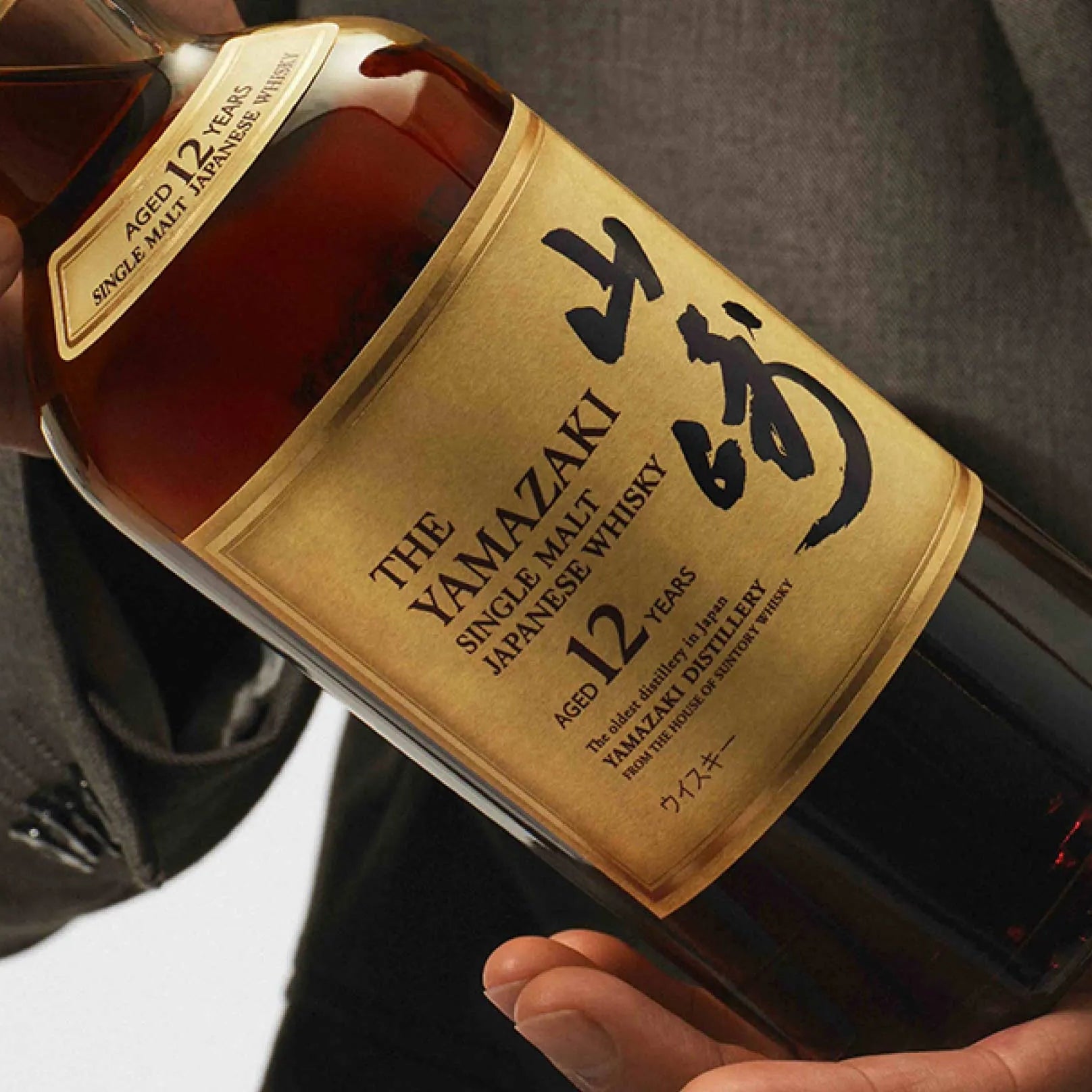 Load image into Gallery viewer, Bottle of Yamazaki whisky held by a person wearing a gray suit.