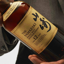 Load image into Gallery viewer, Bottle of Yamazaki whisky held by a person wearing a gray suit.