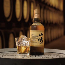 Load image into Gallery viewer, Bottle of Yamazaki whisky with a glass of whisky and ice cubes on a wooden barrel background