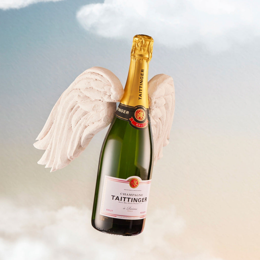 Bottle of Taittinger champagne with angel wings against a cloudy sky background