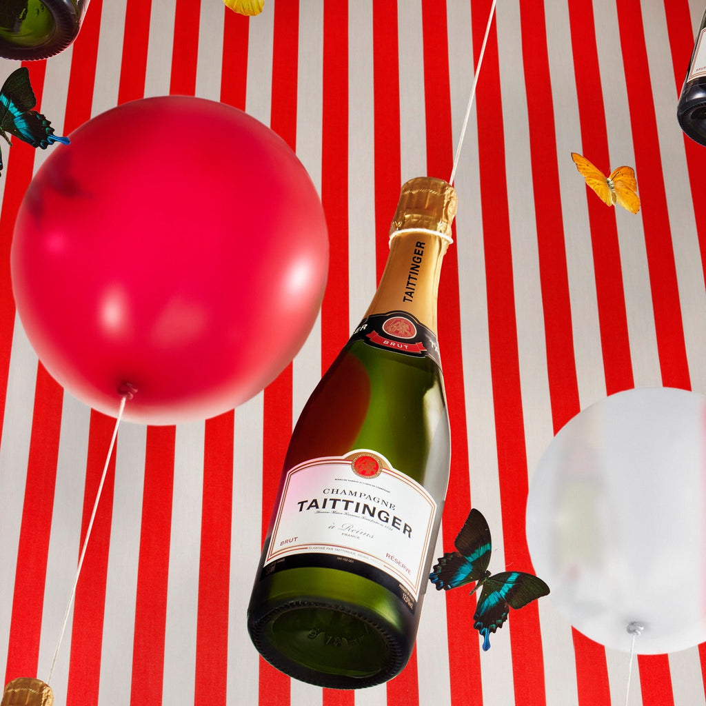 Champagne bottle with Taittinger label on a red and white striped background with balloons and butterflies.