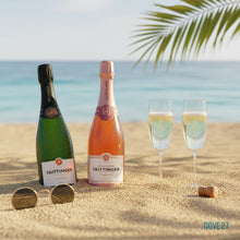 Load image into Gallery viewer, Two bottles of Taittinger champagne on a sandy beach with two glasses and a cork.