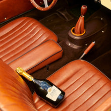 Load image into Gallery viewer, Car interior with brown leather seats, a bottle of Taittinger champagne, and a gear shift.