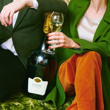 Load image into Gallery viewer, Person holding a bottle of Taittinger champagne and a glass on a patterned surface.