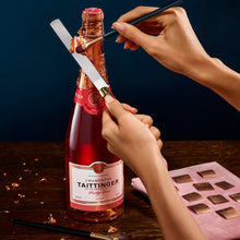 Load image into Gallery viewer, Person opening a Taittinger champagne bottle with a decorative box on a wooden table.