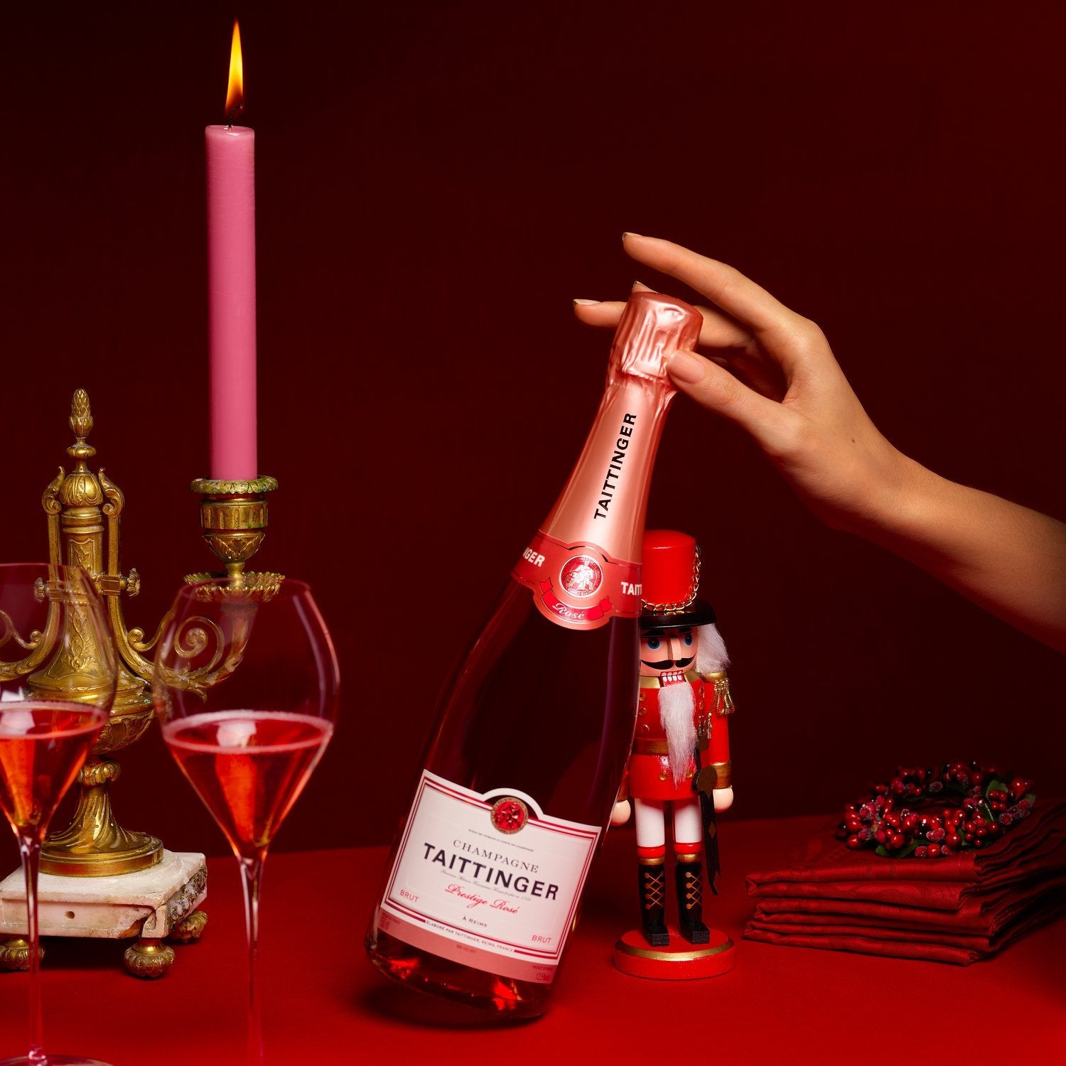 Load image into Gallery viewer, Bottle of Taittinger champagne on a red surface with a hand holding it, candles, and glasses in the background.