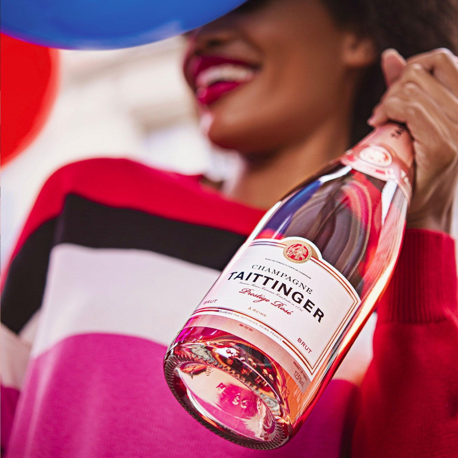 Load image into Gallery viewer, Woman holding a bottle of Taittinger champagne with a colorful background