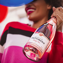 Load image into Gallery viewer, Woman holding a bottle of Taittinger champagne with a colorful background